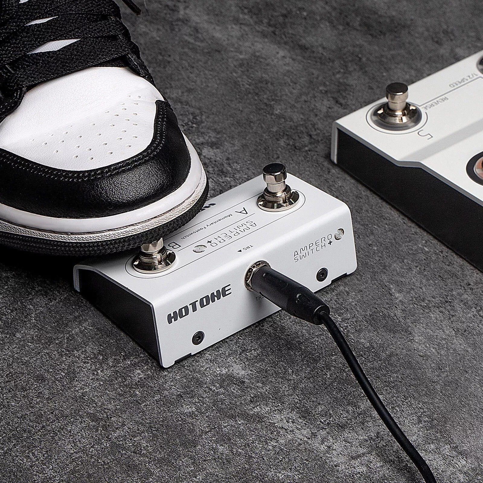 Sneaker pressing a footswitch on the Hotone FS-2 Ampero Switch+ on a concrete floor