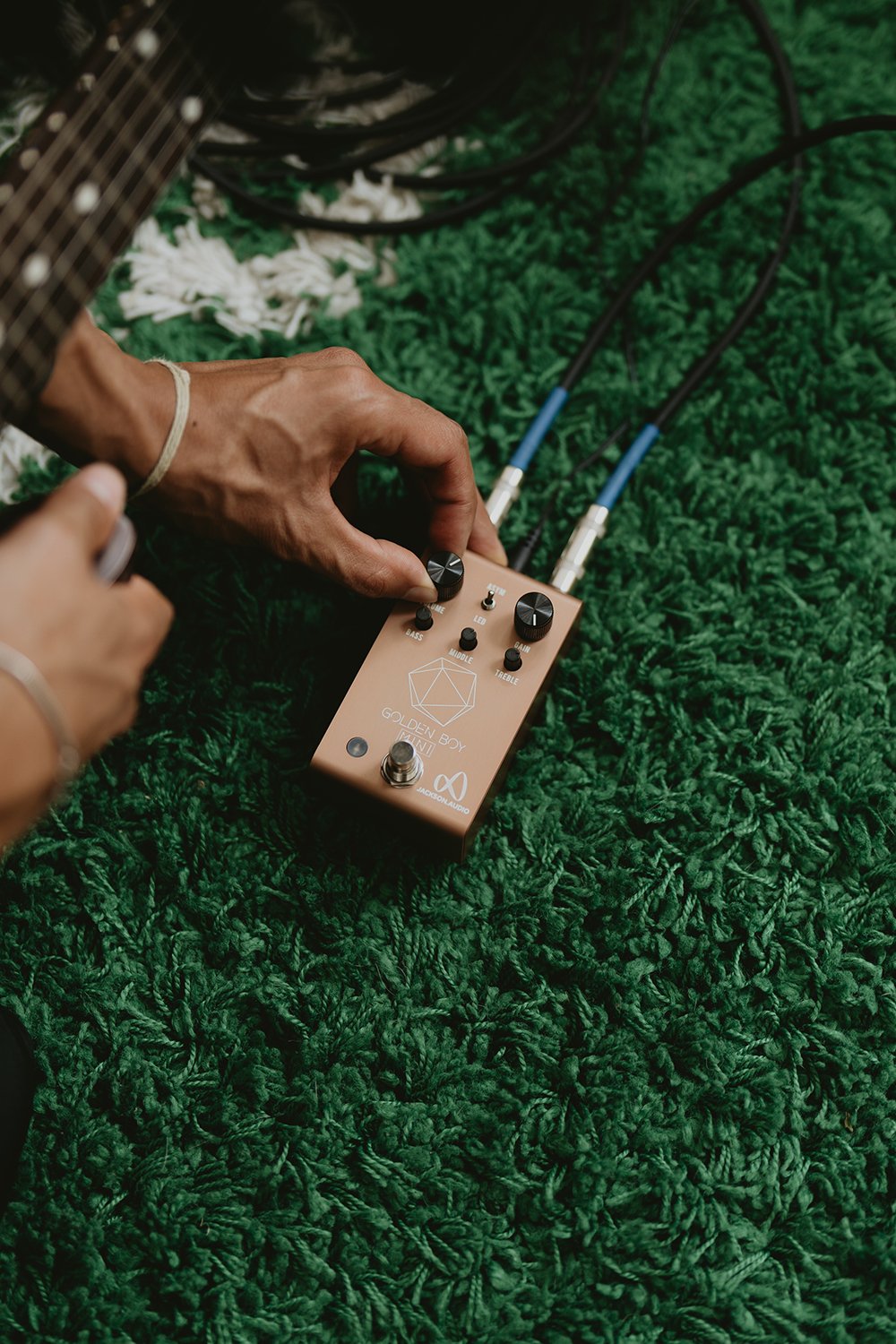 Jackson Audio Golden Boy Mini Transparent Overdrive, Lifestyle photo of a hand connecting a cable to the Golden Boy Mini on grass outdoors.