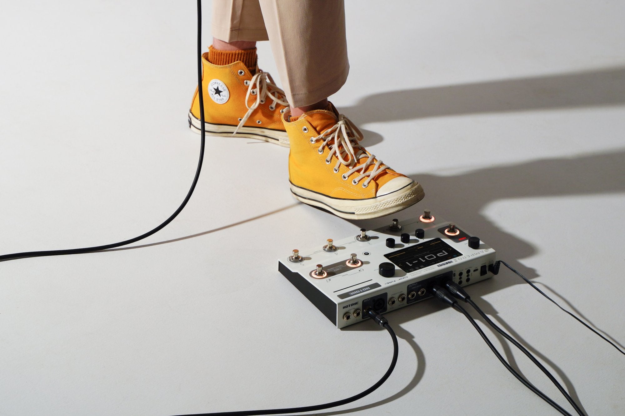 Feet beside a white Hotone Ampero II Press expression pedal with cables connected on the floor