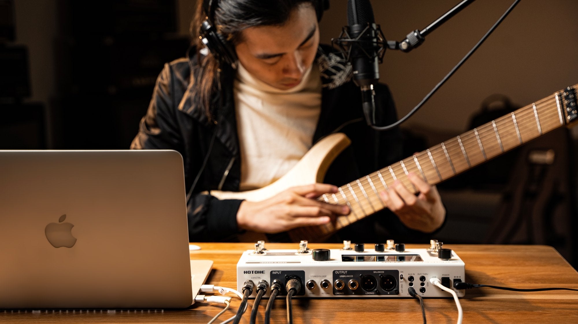 Musician recording electric guitar through an audio interface and laptop in a home studio