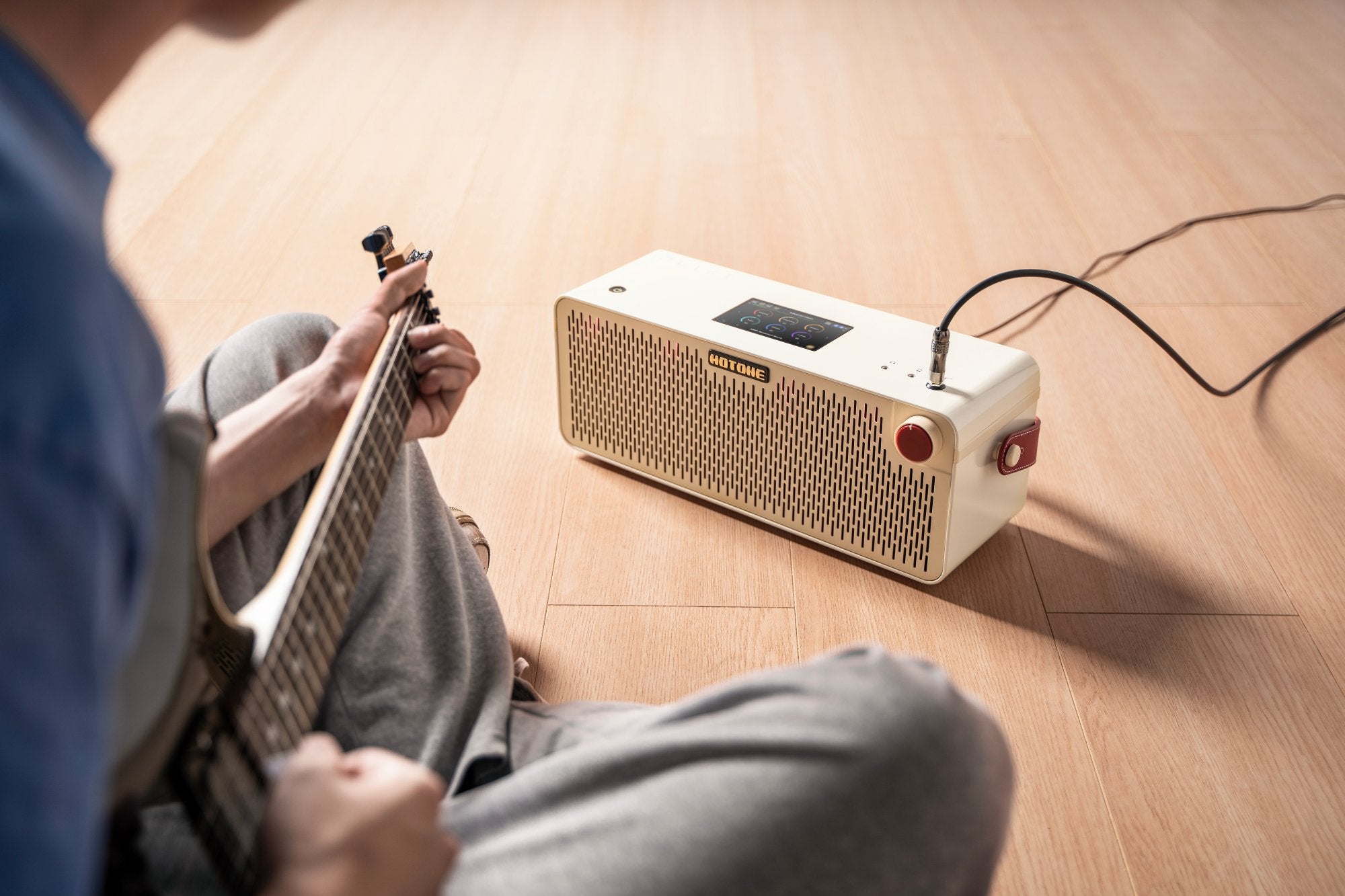 Person playing electric guitar through a Hotone Pulze amplifier at home