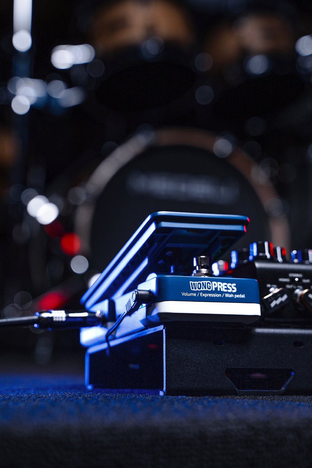 Hotone SP-21 Wong Press pedal on stage under blue lighting near a drum kit