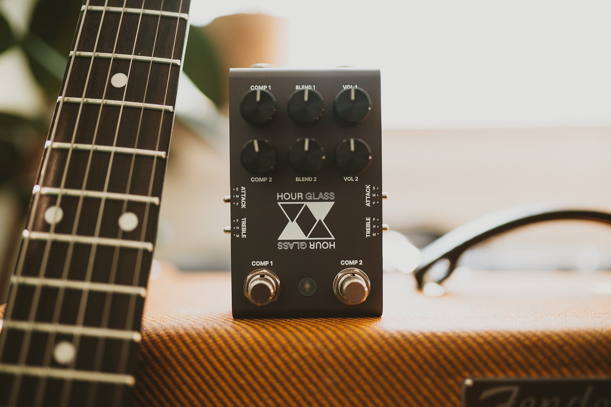 Jackson Audio Hour Glass Analog Dual Compressor Pedal, Lifestyle photo of the Hour Glass pedal positioned beside a guitar neck resting on a chair.
