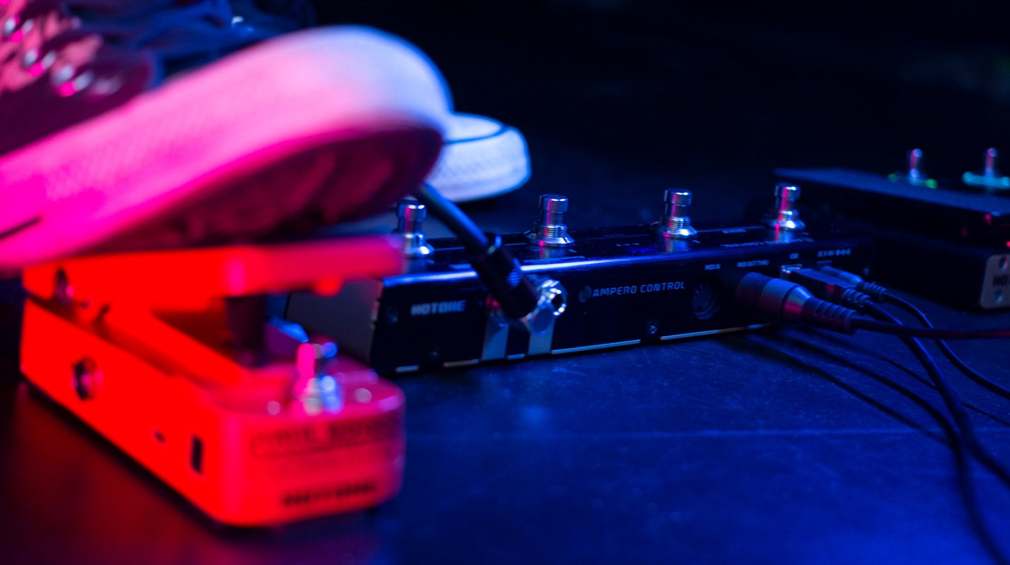 Foot pressing a footswitch on a pedalboard with the Hotone Ampero Control EC-4, stage lighting