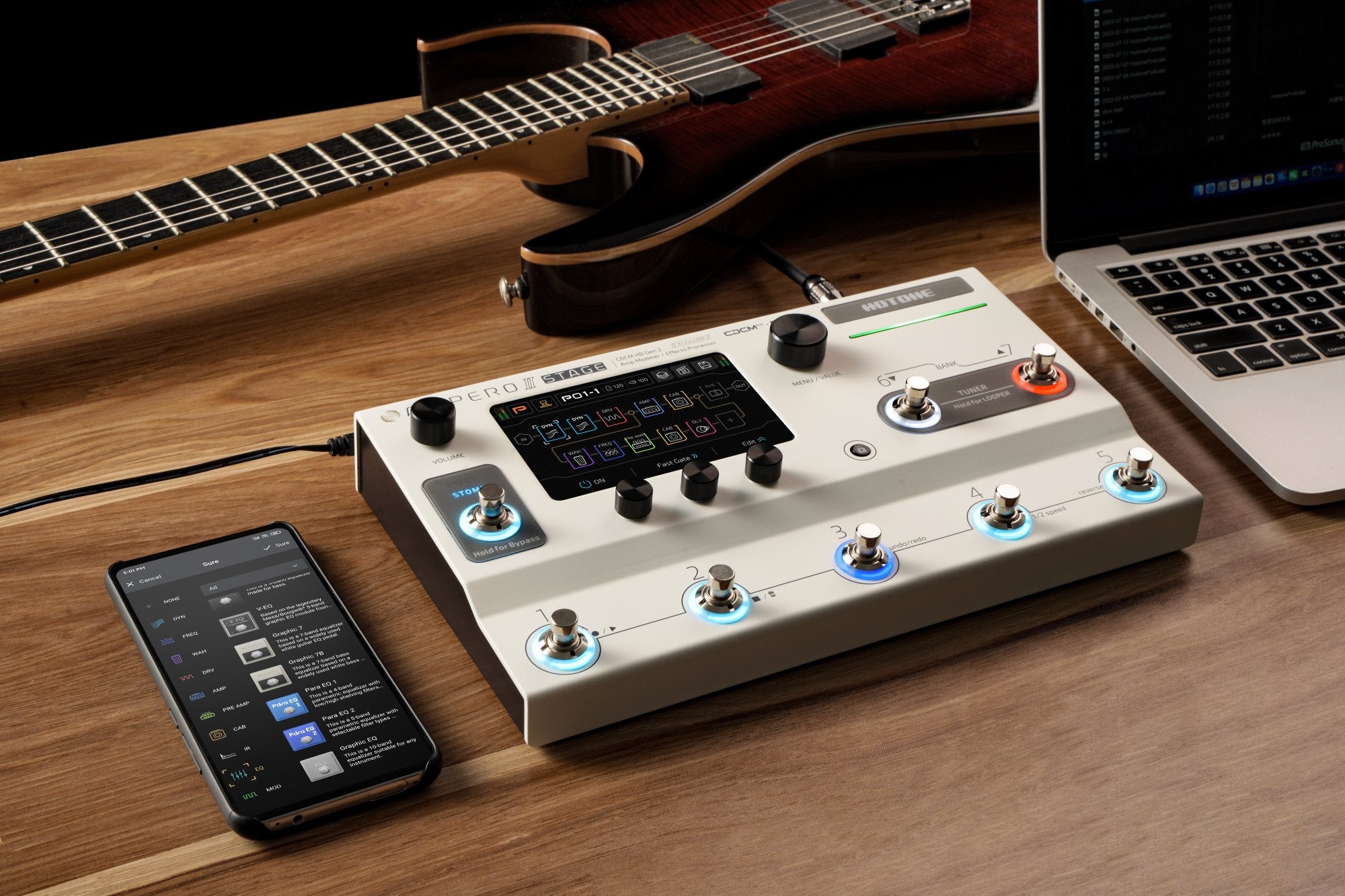 Hotone Ampero II Stage amp modeler on a desk with guitar, phone and laptop in a home studio setup