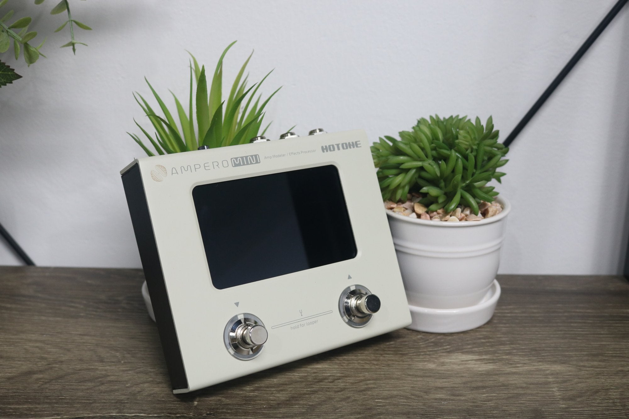 Hotone Ampero Mini amp modeler displayed on a wooden table beside a small plant