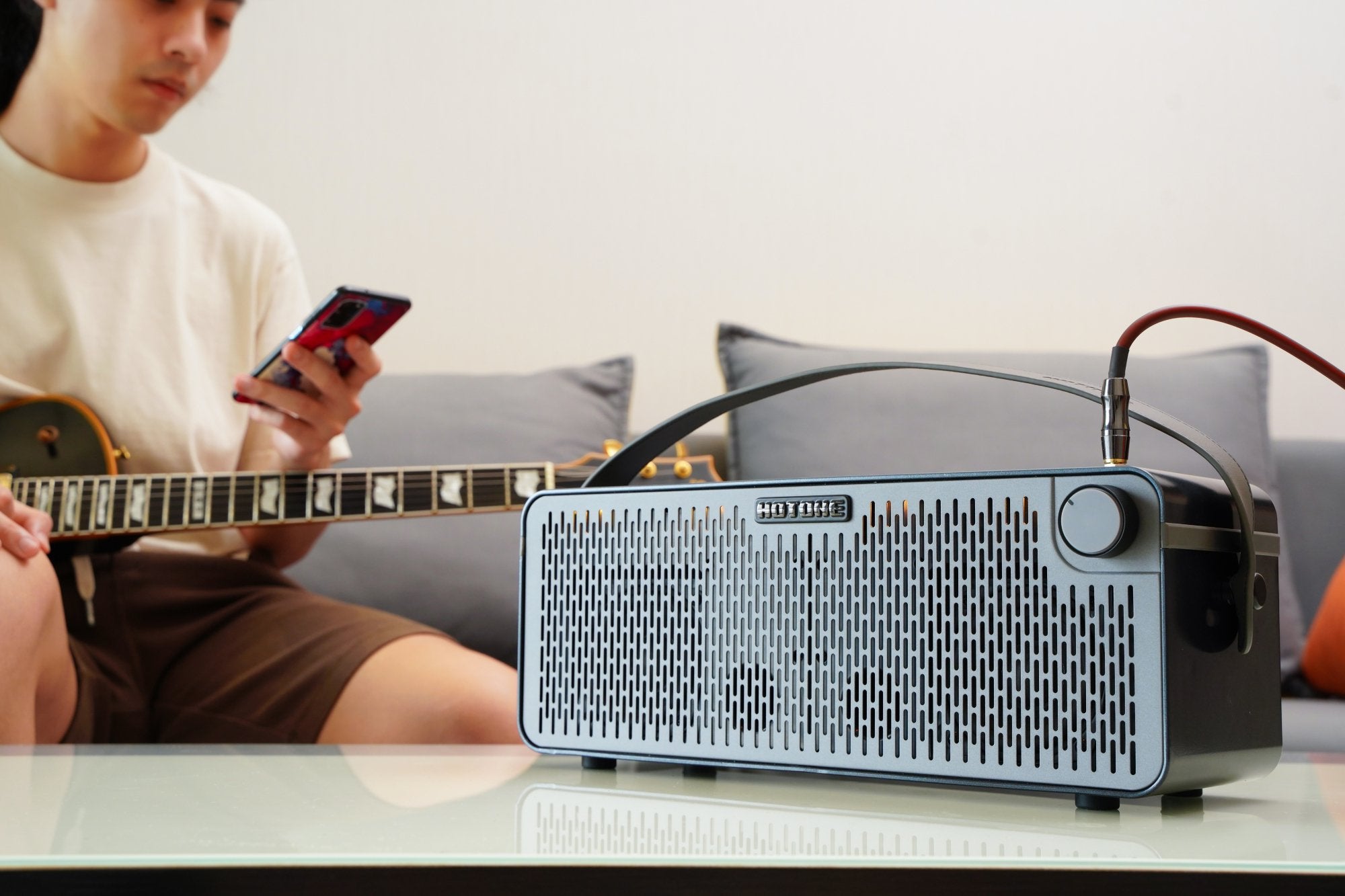 Person playing guitar beside a Hotone Pulze AP-30BK amplifier on a glass table