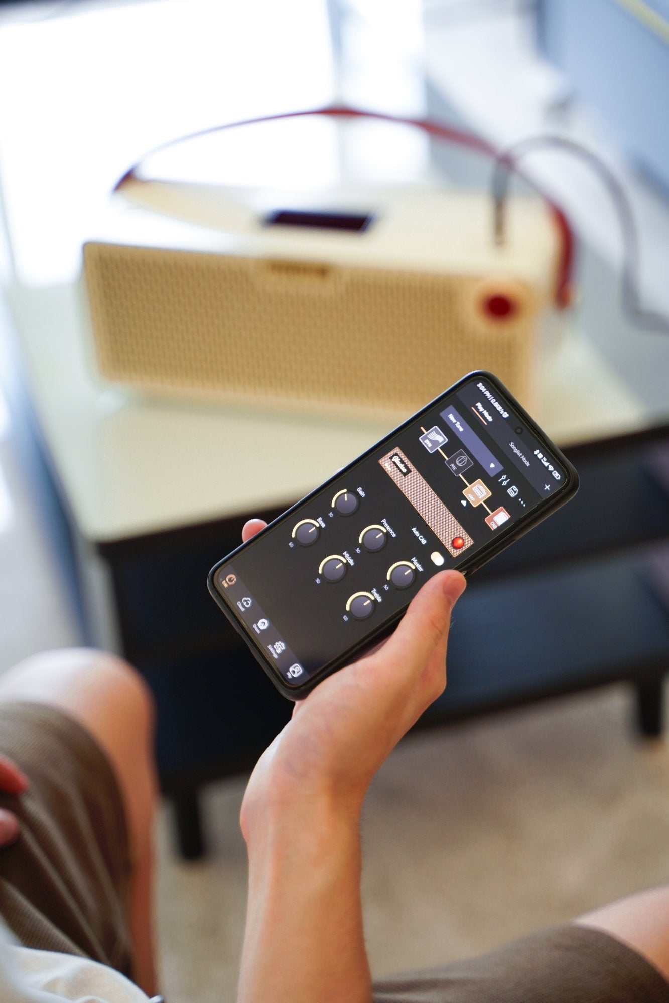 Hand holding a smartphone with the Hotone Pulze companion app, amplifier in background